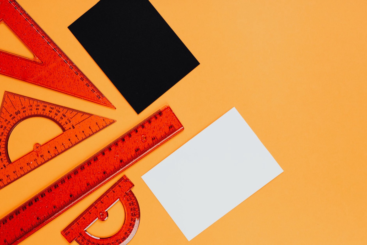 Vibrant orange rulers and geometric tools on an orange background with black and white cards.
