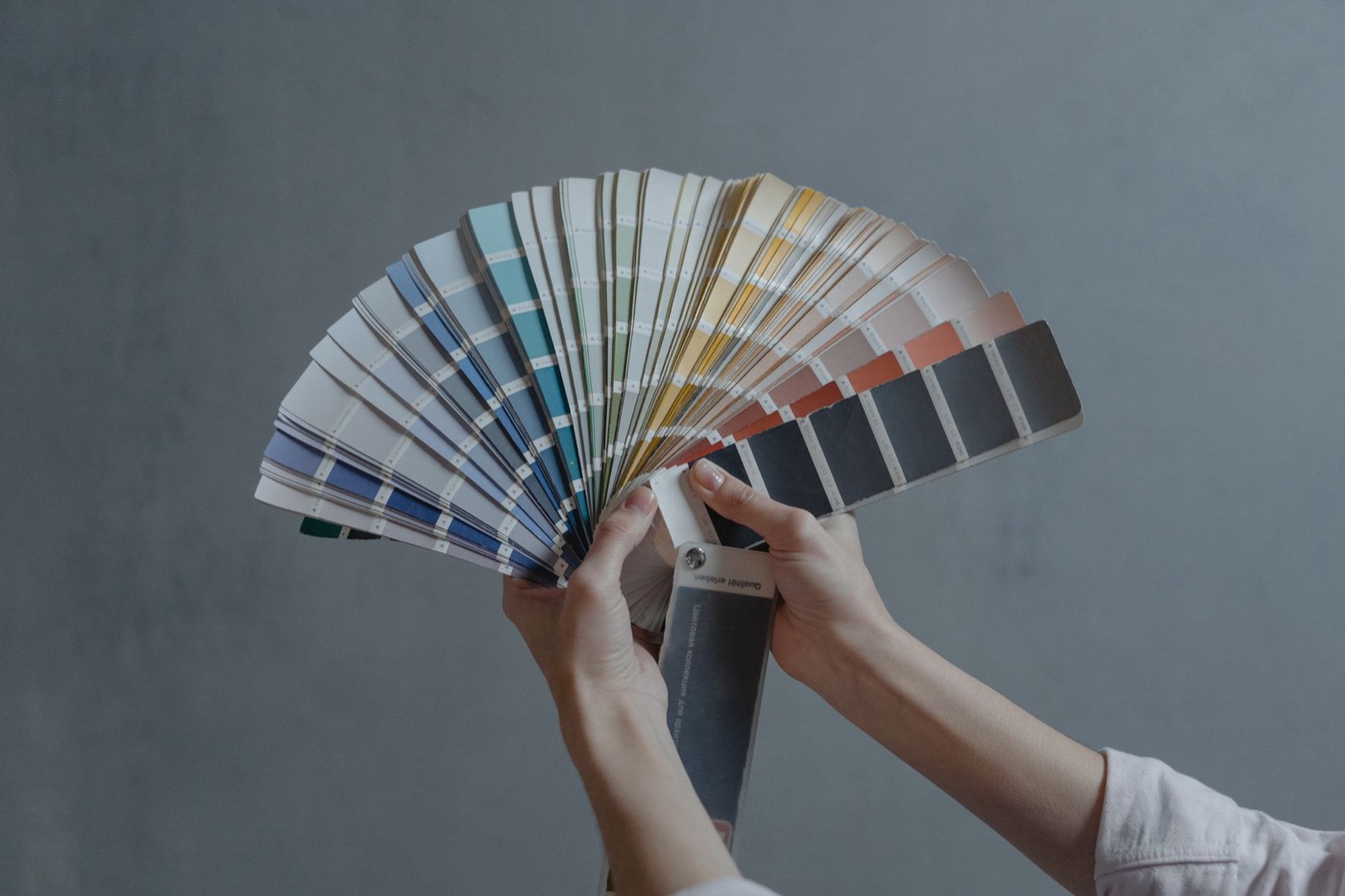Hands holding a colorful fan of swatches on a gray backdrop.