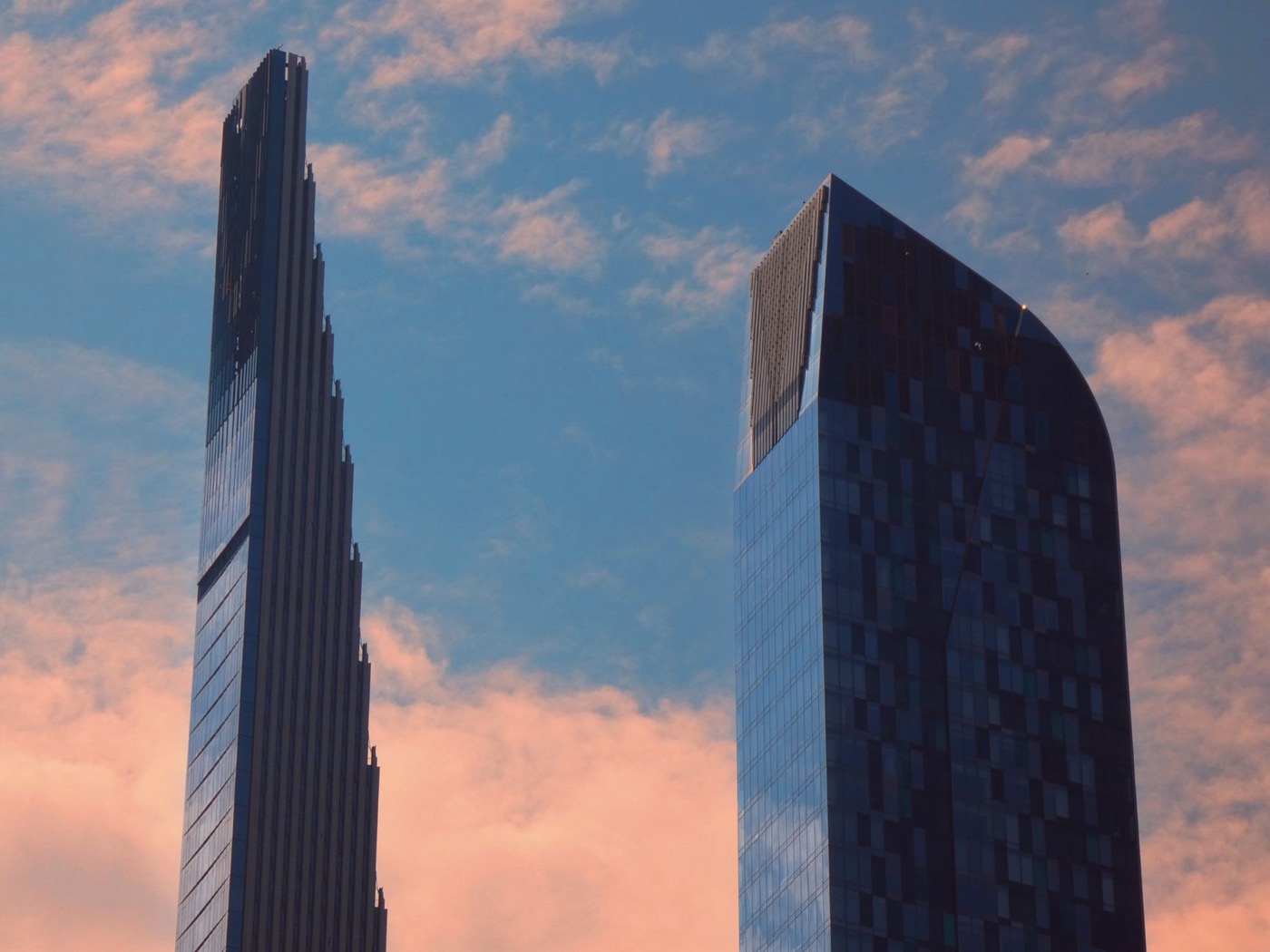 Elegant New York skyscrapers stand tall against a vibrant blue sky with pink clouds.