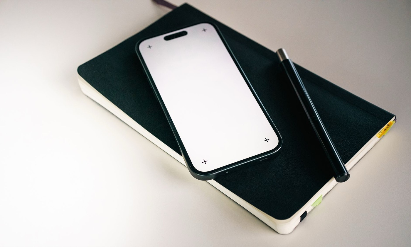 Minimalist flat lay featuring a smartphone, notebook, and pen.