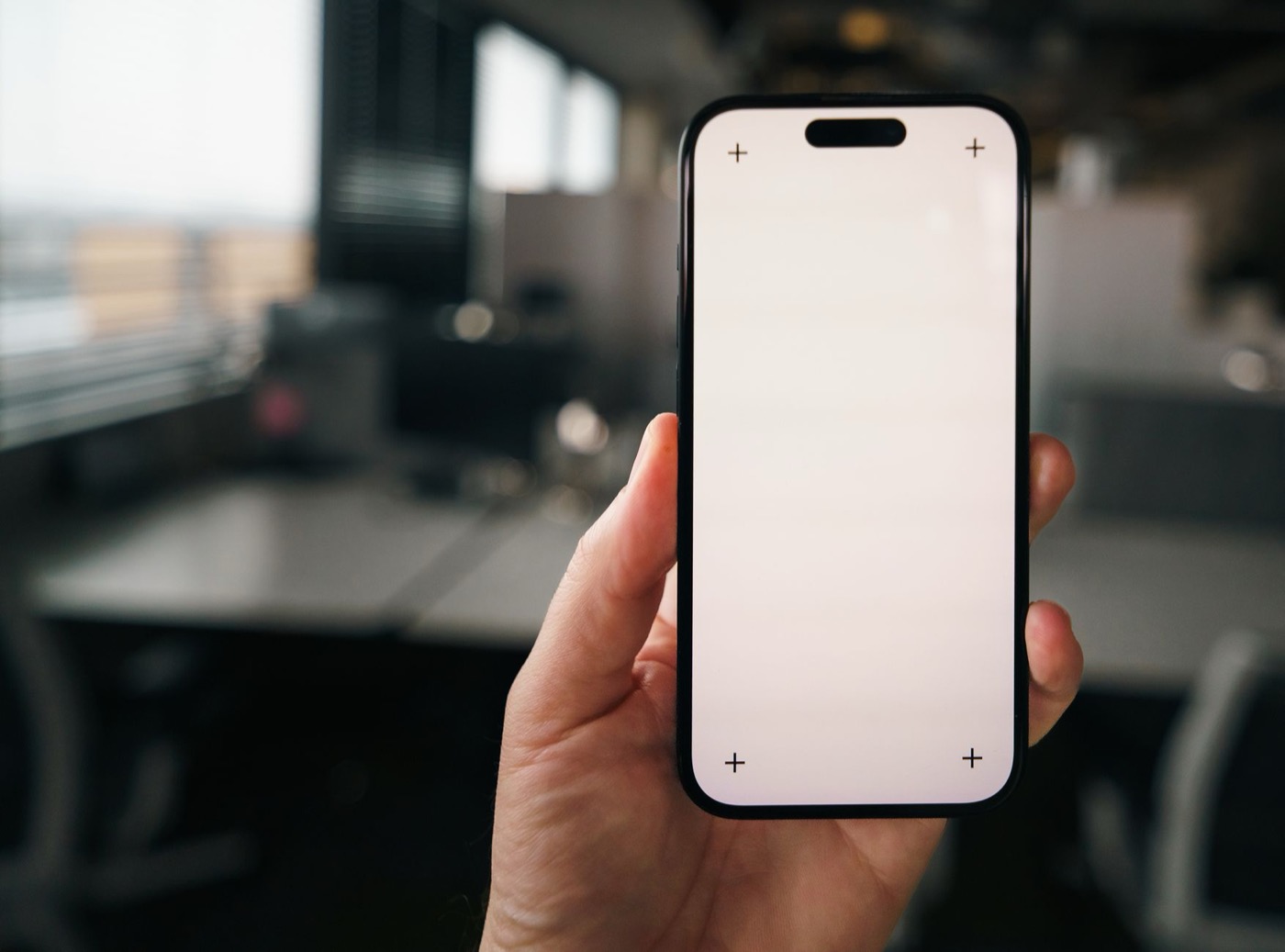 Hand holding a blank smartphone screen mockup in a modern office environment.