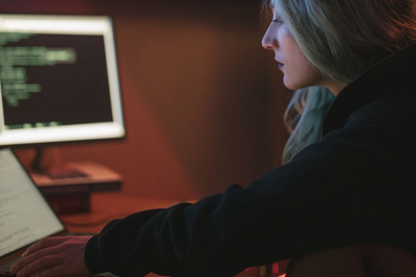A woman working late on a laptop with code displayed on the screen in a dark room.