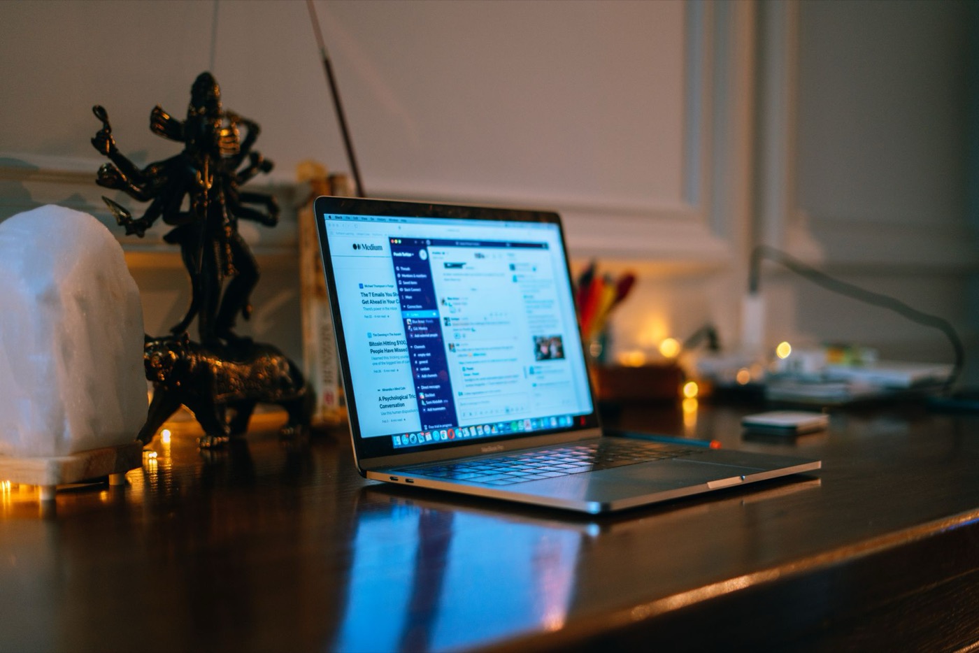 A cozy home office setup with a laptop on a wooden desk surrounded by warm lighting and decor.