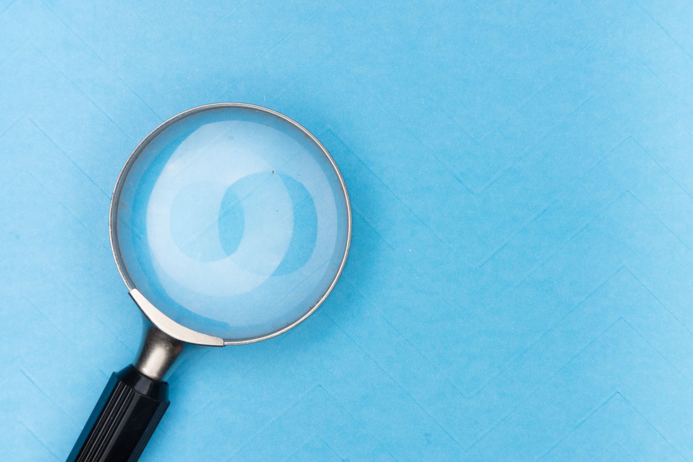 Close-up of a magnifying glass on a blue surface.