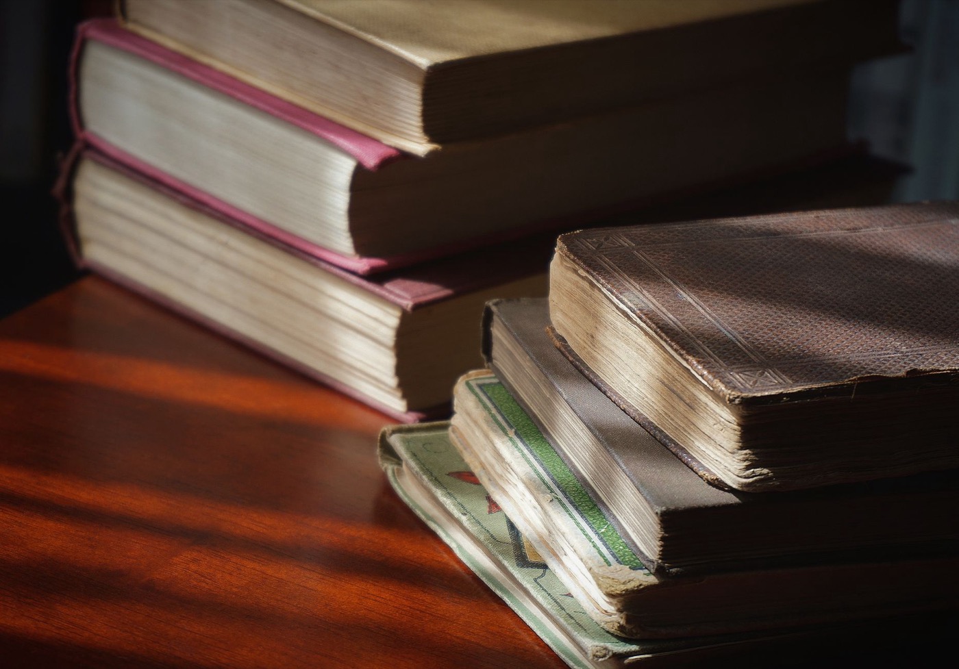 A close-up of vintage books stacked on a wooden table, showcasing aged pages and covers.