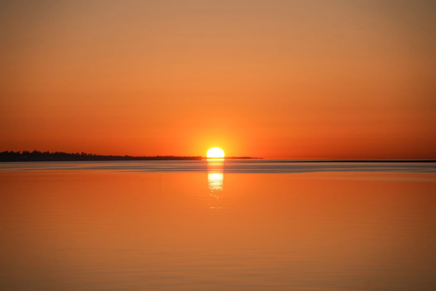 A tranquil sunrise over a calm ocean, casting a warm golden reflection on the water.