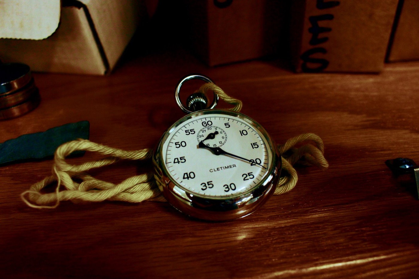 Close-up of an antique silver stopwatch resting on a wooden table with a yellow rope.