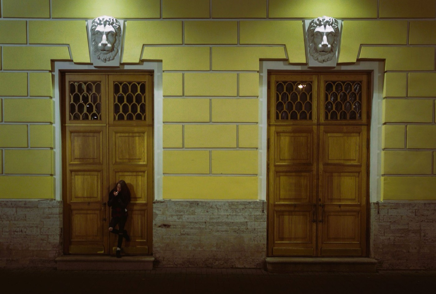 Nighttime scene of a person standing by illuminated wooden doors.