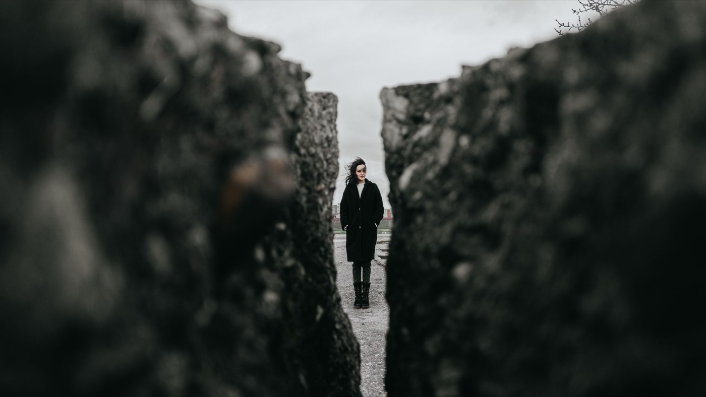A woman with brown hair stands between rocky walls on a windy, cloudy day.