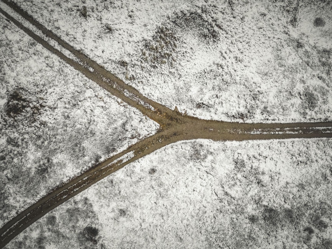 Drone shot of a snowy landscape with a forked dirt road in Bindslev, Denmark.