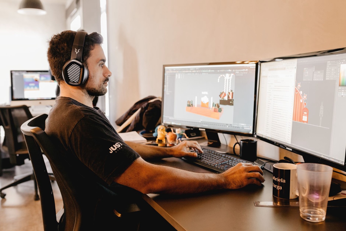 A man wearing headphones works on a computer with two monitors in a modern office setup.